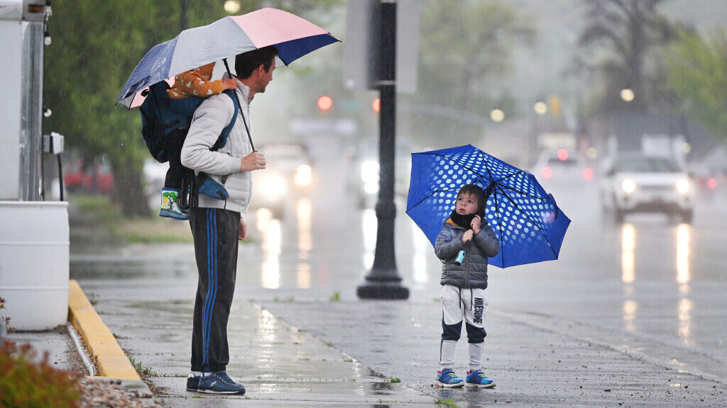 A man holds a red umbrella over himself and one of his children in the rain. A second child holds a...