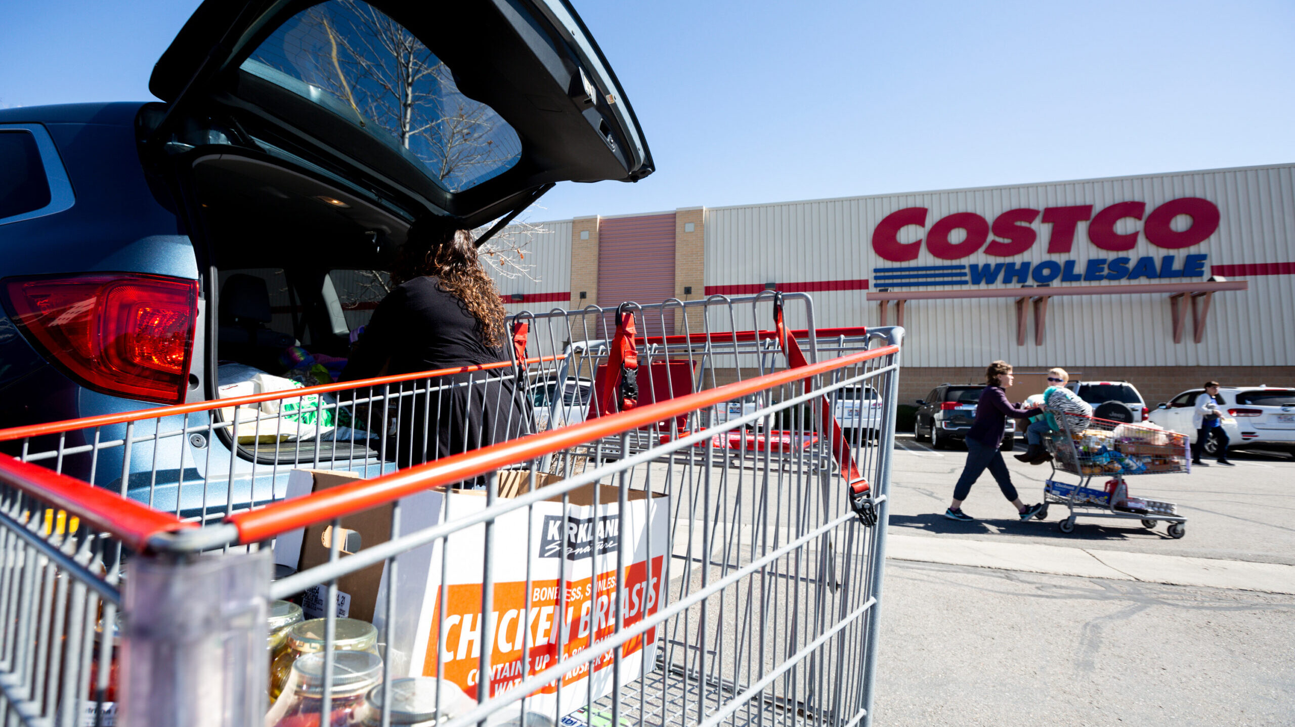 a woman loads groceries into her car from costco, costco membership fees are increasing...