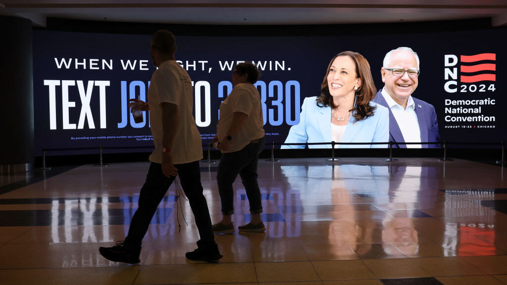 dnc poster hangs at united center as people walk past...