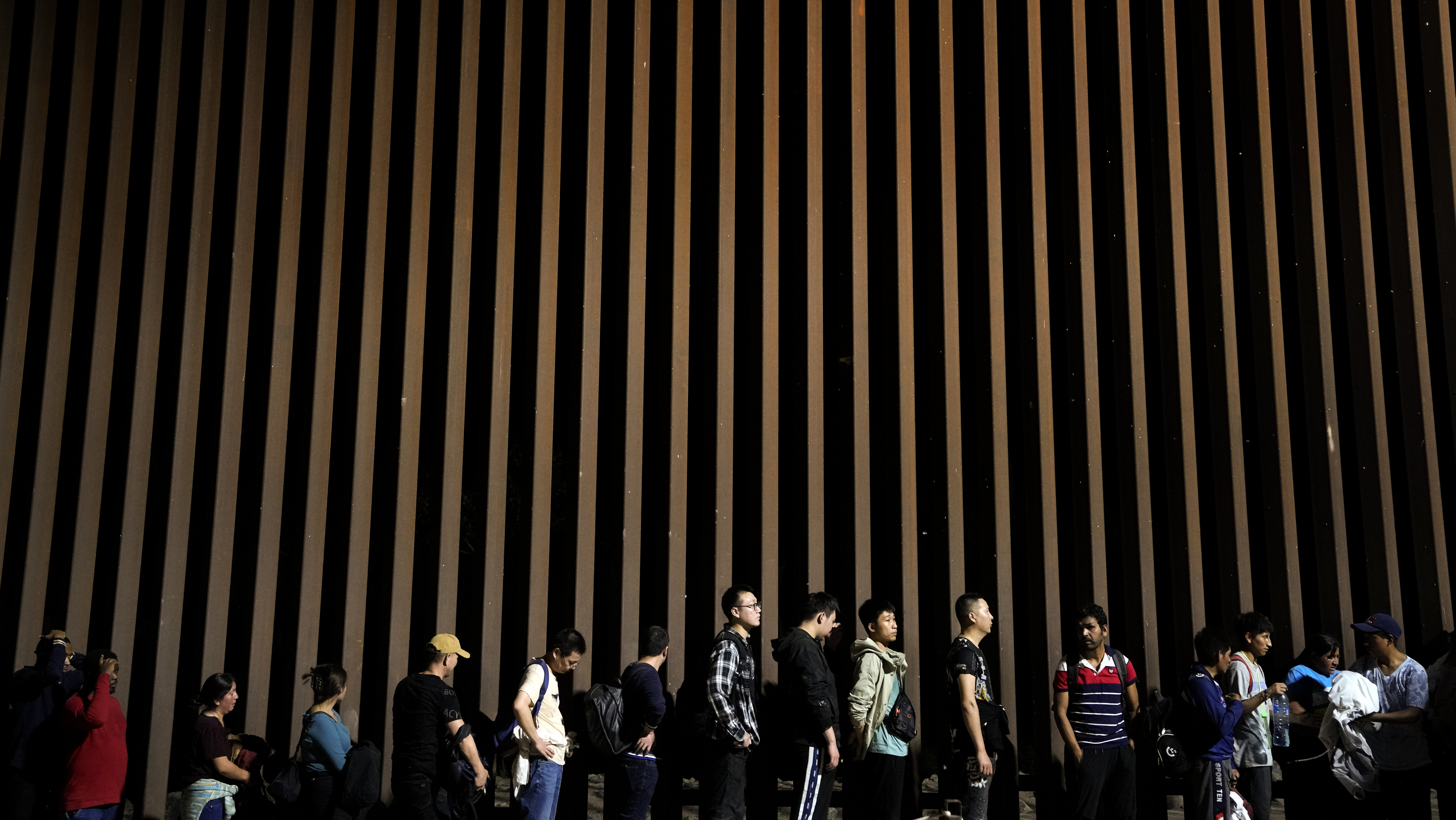 FILE - People line up against a border wall as they wait to apply for asylum after crossing the bor...