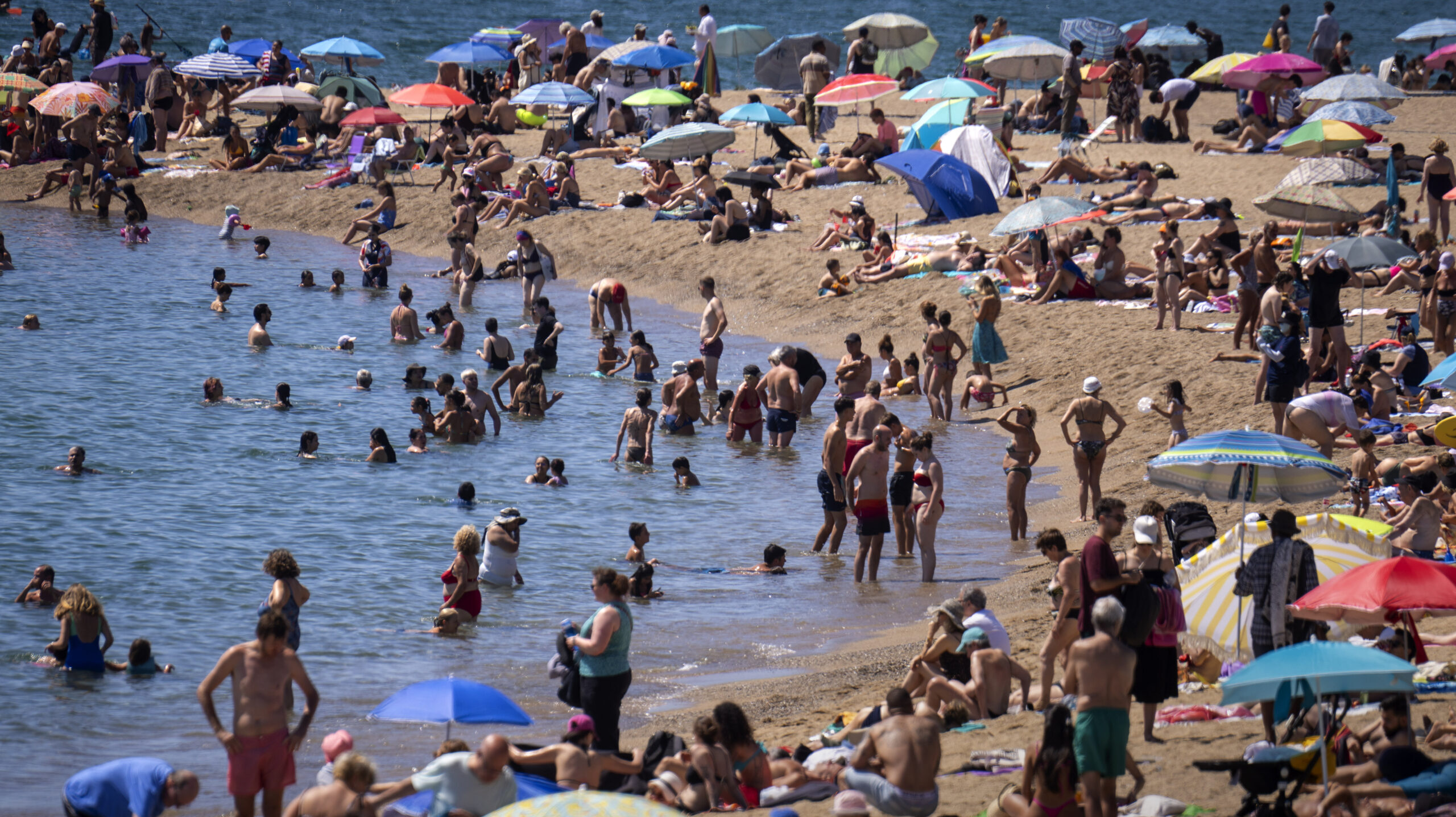 Bathers cool off in the water while others sunbathe on a Barcelona beach,...