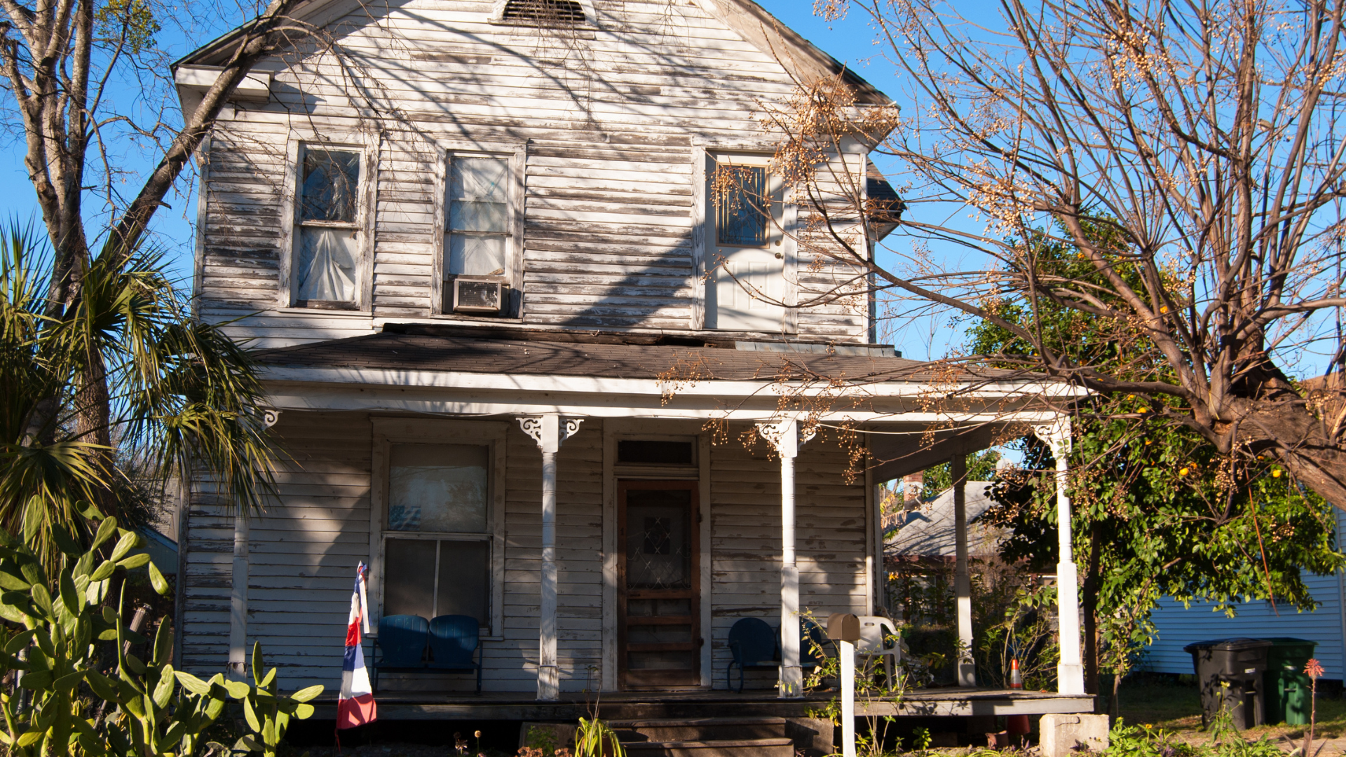 An old, white house sits in front of a blue sky....