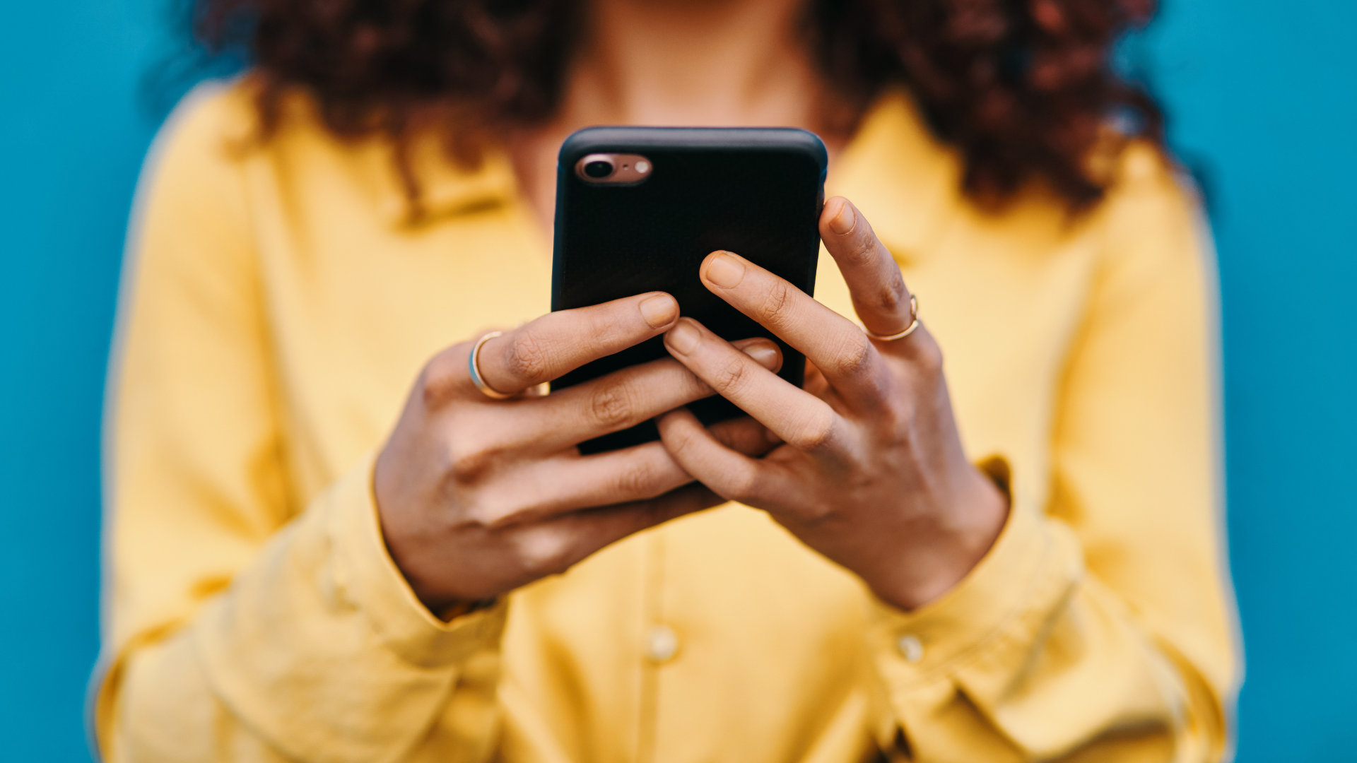 A person wearing a yellow shirt looks at a smartphone....